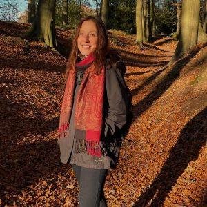 woman standing in a beech wood with a red scarf
