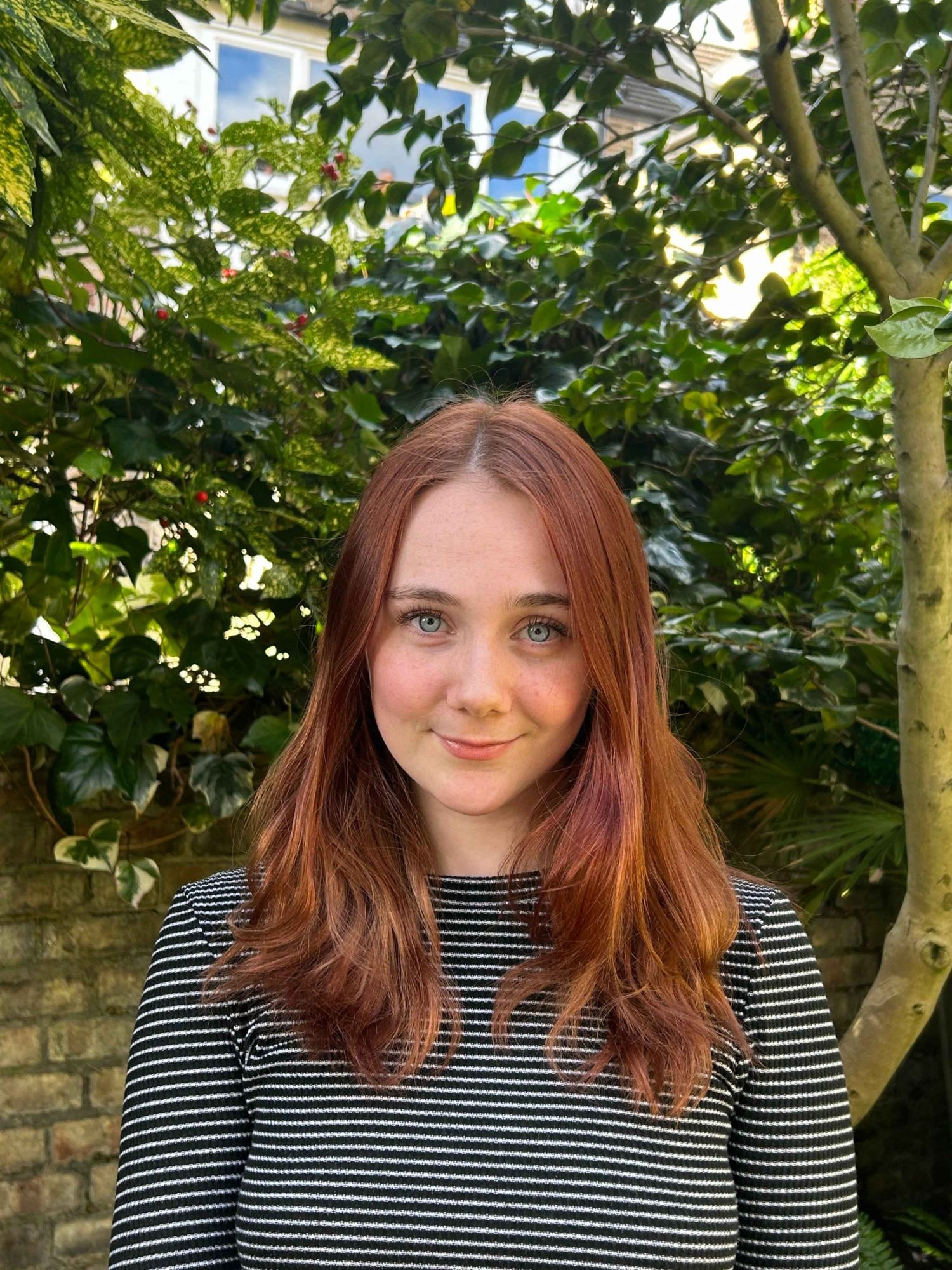 Profile photo of woman with red hair and stripey top looking at camera